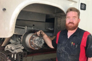A D&D Service Center mechanic standing next to a dismantled brake underneath a vehicle in Girard, IL.
